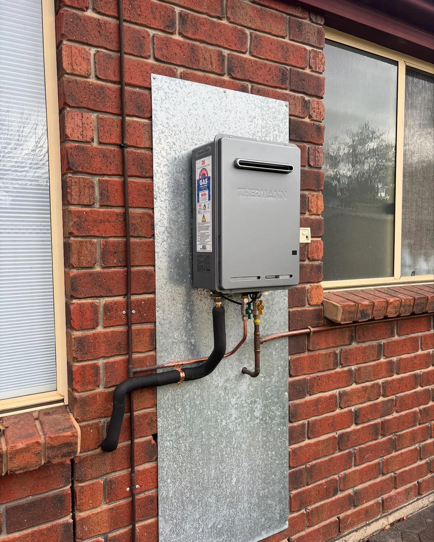 R&J continuous-flow hot-water installation on an exterior brick wall