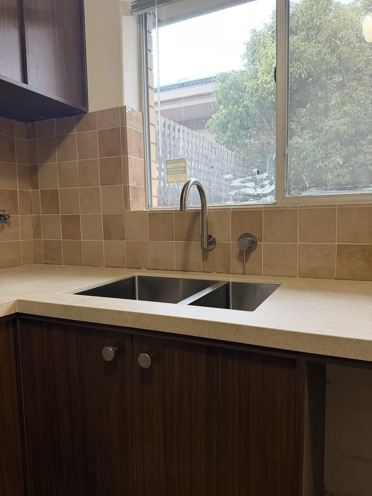 Double stainless kitchen sink with a gooseneck mixer under a window