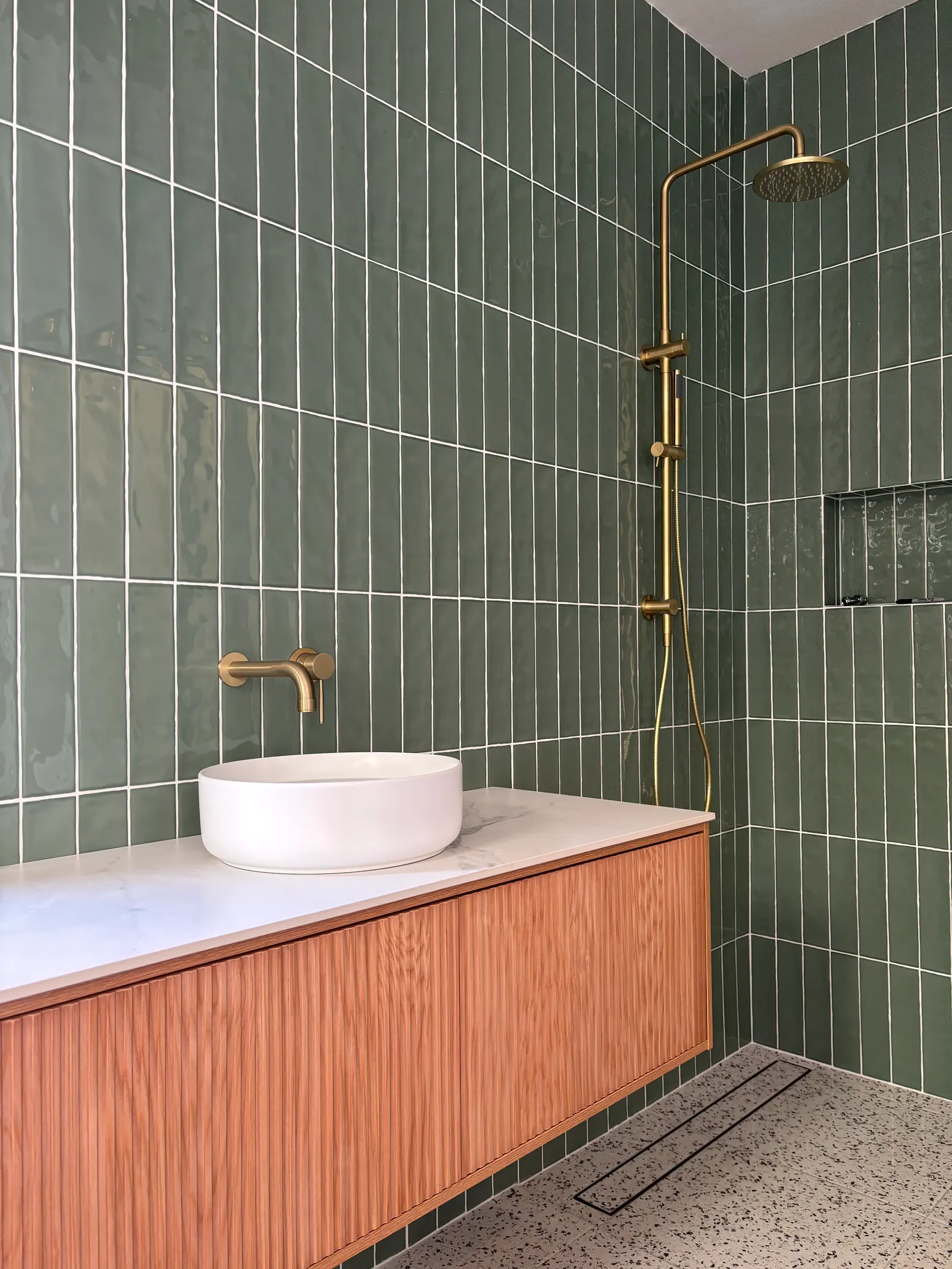 Sage tiled bathroom with a timber vanity and brass shower fittings